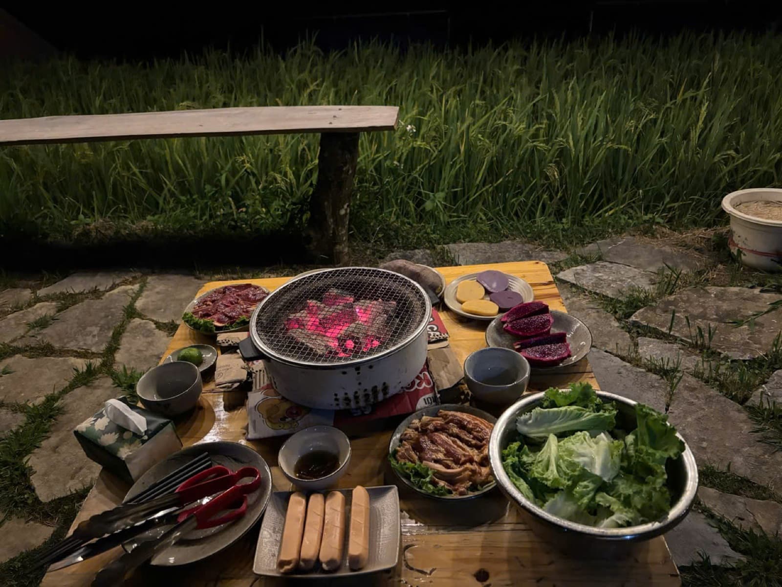 A charcoal grill with meat and vegetables outdoors at night
